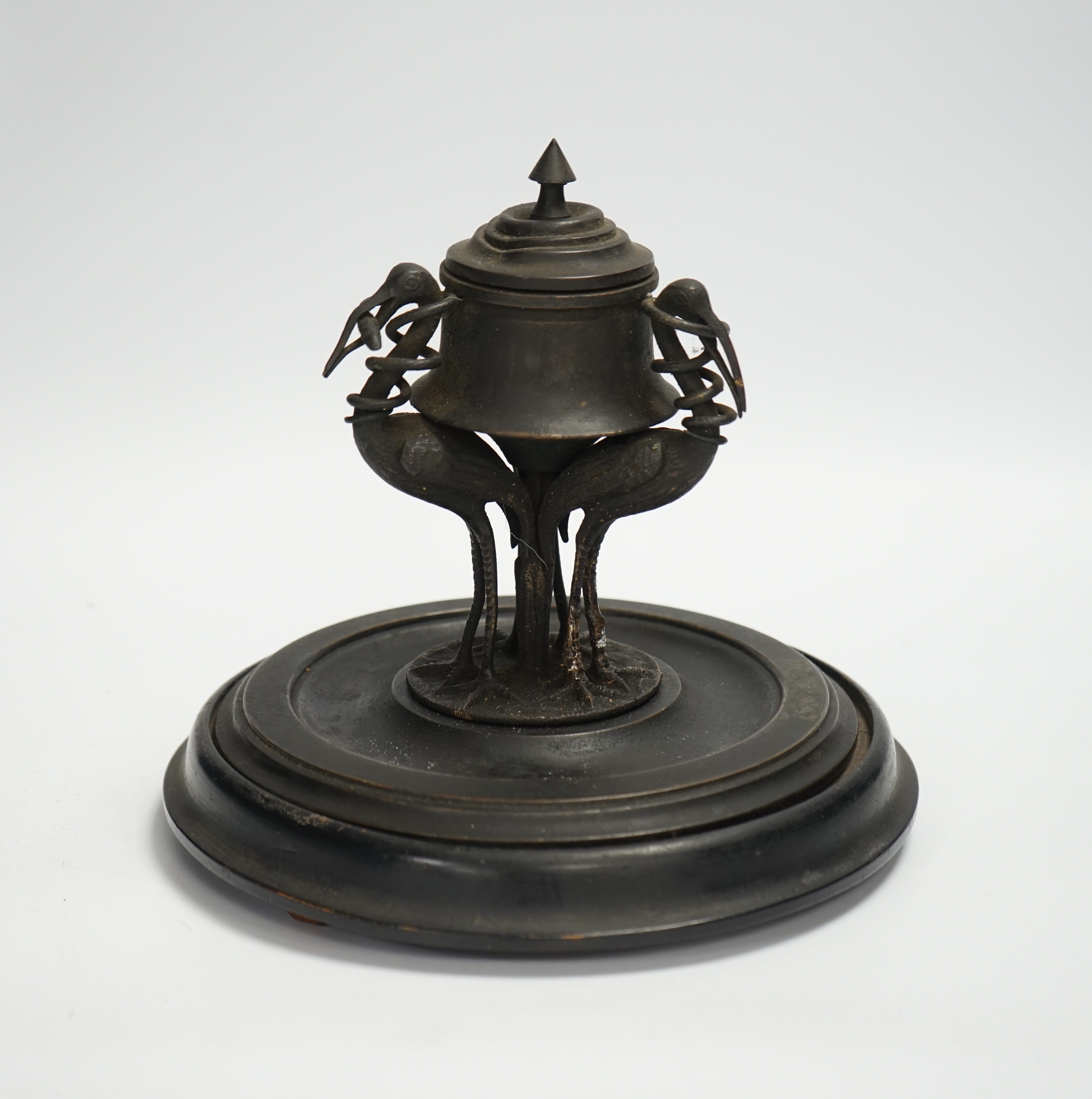 A late 19th century patinated metal inkwell, modelled with three cranes on an ebonised pine base, 18cm